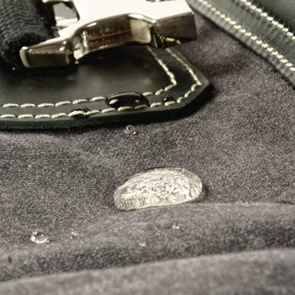 Water-resistant waxed canvas backpack with water droplets beading on the material beside the leather buckle patch
